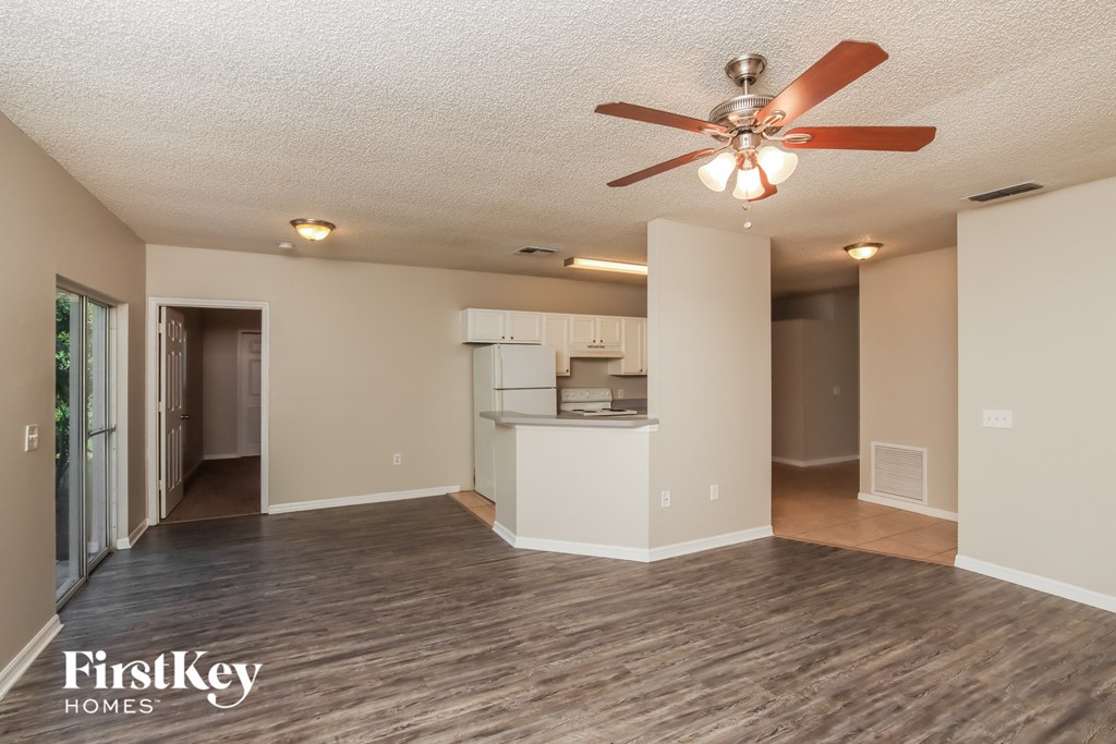 an empty living room with a ceiling fan and a kitchen