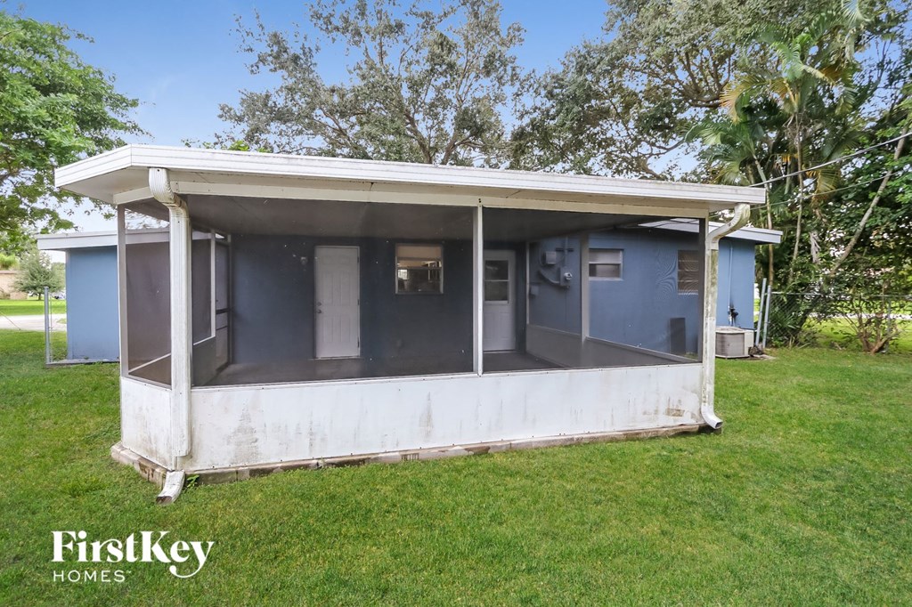 A blue and white house with a porch is surrounded by grass and trees.
