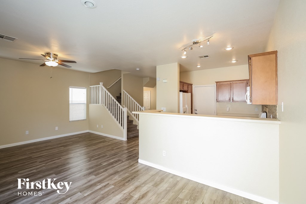 an empty living room with a kitchen and a ceiling fan
