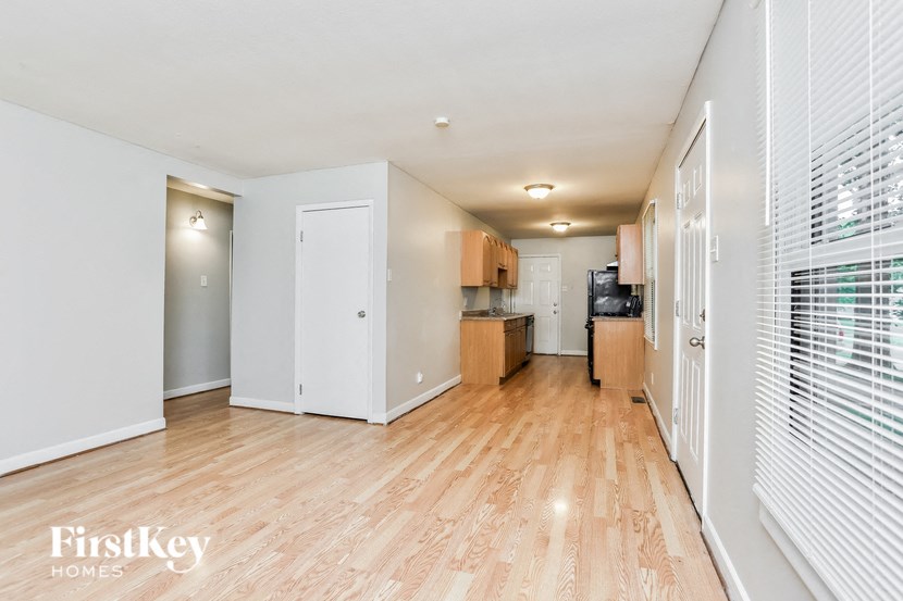 A spacious room with wooden floors and white walls, featuring a kitchenette with a refrigerator, oven, and cabinets.