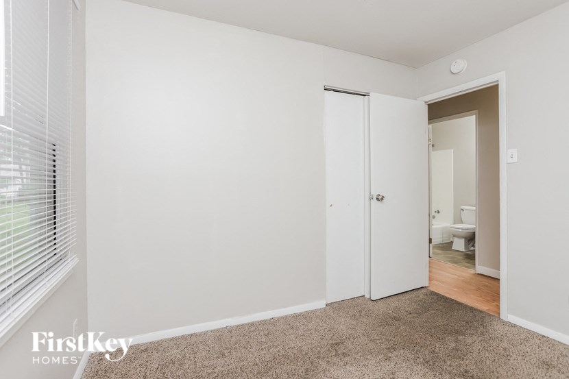A carpeted room with a white door and a window with blinds.