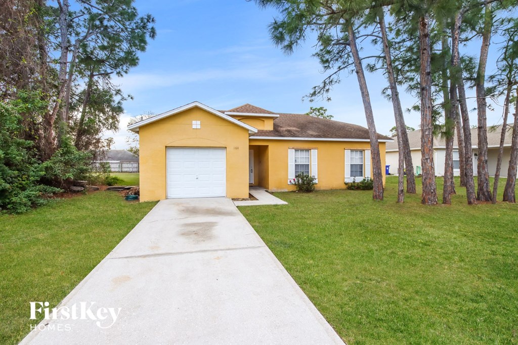 A yellow house with a white garage door is surrounded by greenery.