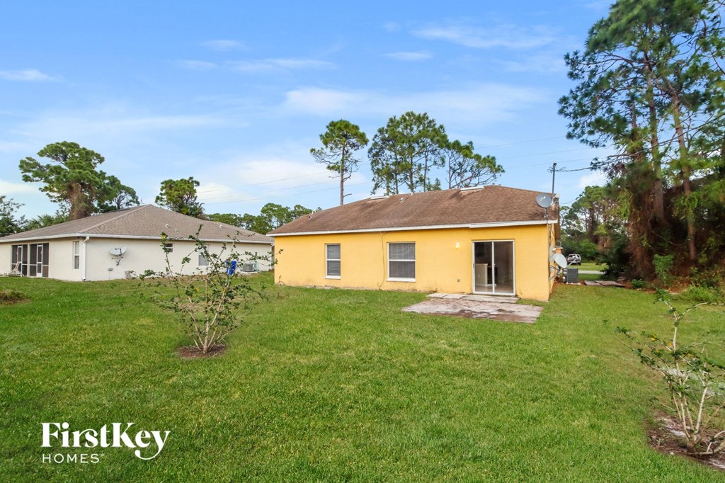 A yellow house with a white house in the background and trees around.