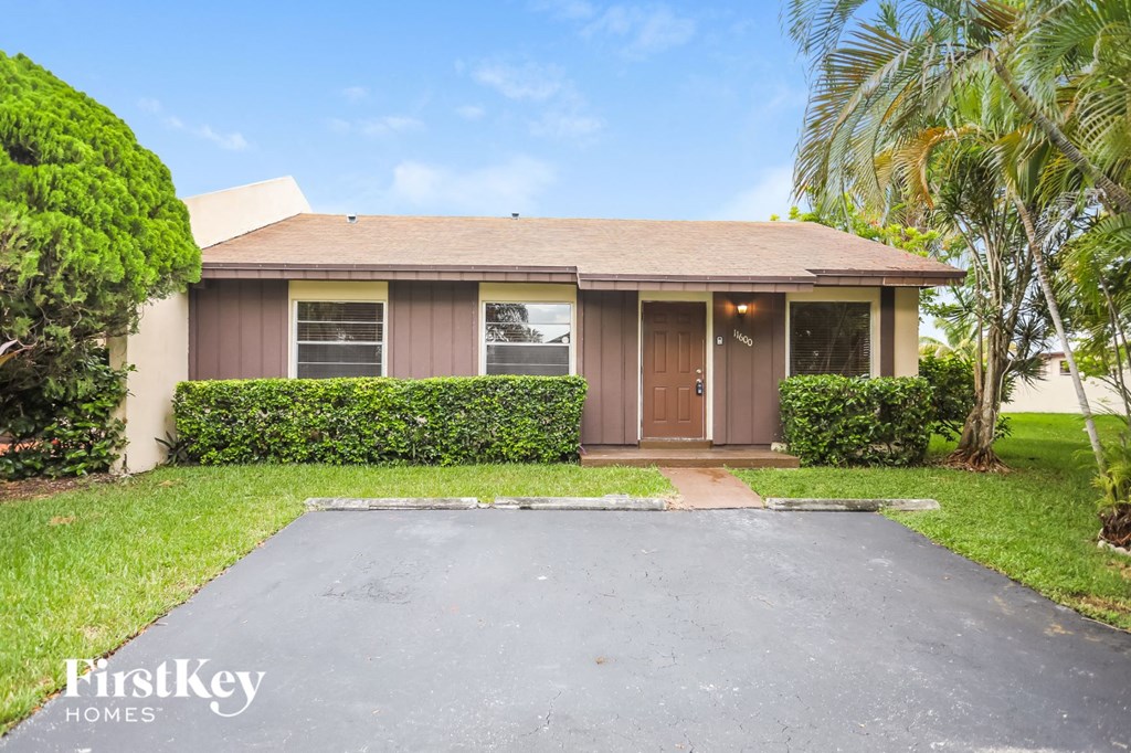 a small brown house with a driveway and palm trees