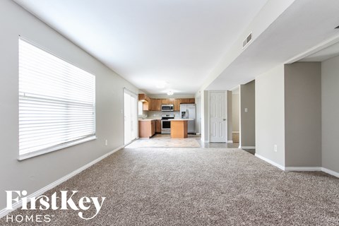 A spacious room with a carpeted floor and a kitchen area in the background.