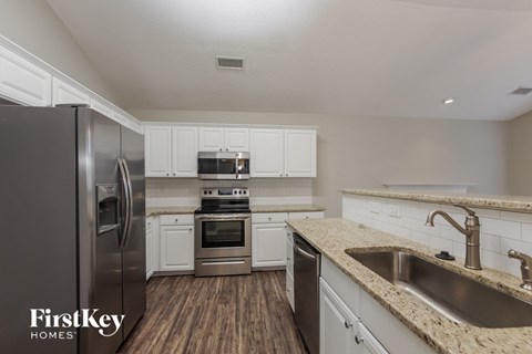 A kitchen with a stainless steel refrigerator and a sink with granite countertops.