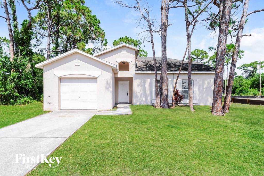 A white house with a garage is surrounded by trees.