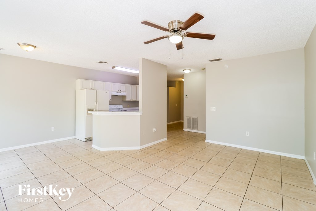 A spacious room with a ceiling fan and a kitchenette in the background.