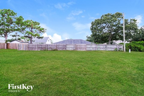 A grassy field with a fence and trees in the background.