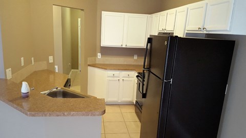 A black refrigerator sits in a kitchen with white cabinets.