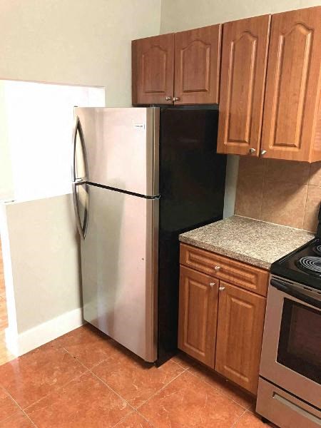 A black refrigerator is in a kitchen with brown cabinets and a stove.