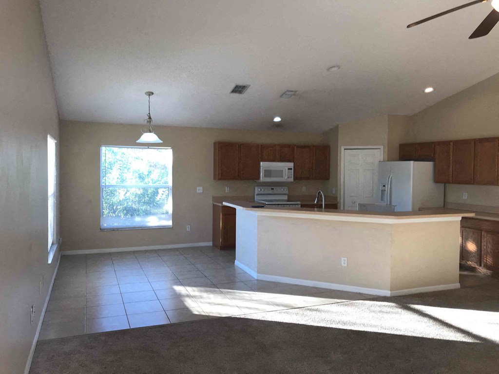 A kitchen with a white fridge and microwave, brown cabinets, and a ceiling fan.