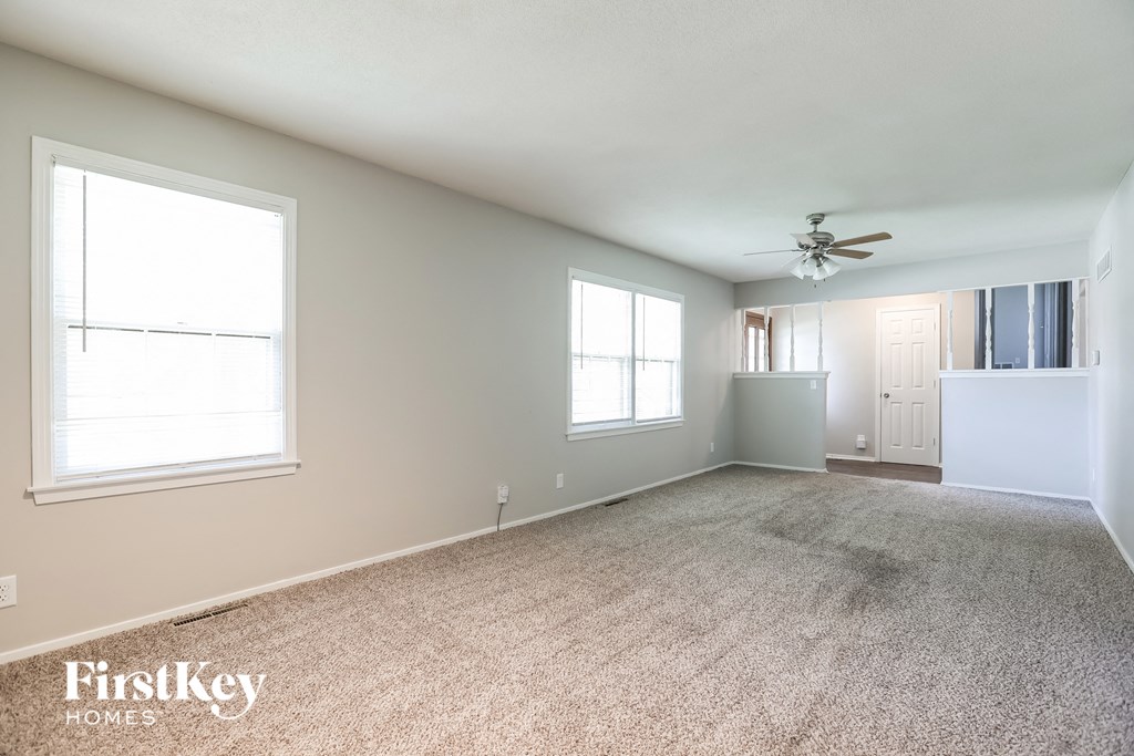 A spacious room with a carpeted floor, a ceiling fan, and a door leading to another room.
