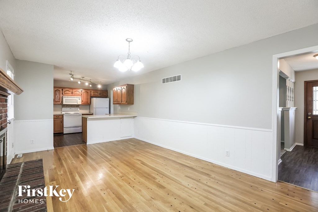 A large empty room with wooden floors and a kitchen in the background.