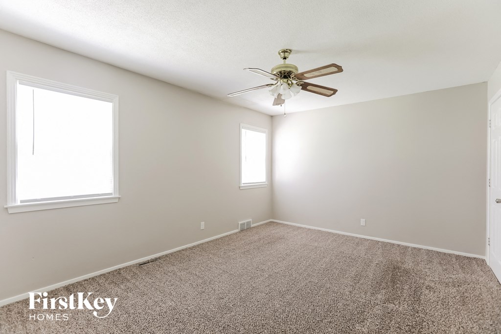 A room with a carpet floor, a ceiling fan, and two windows.
