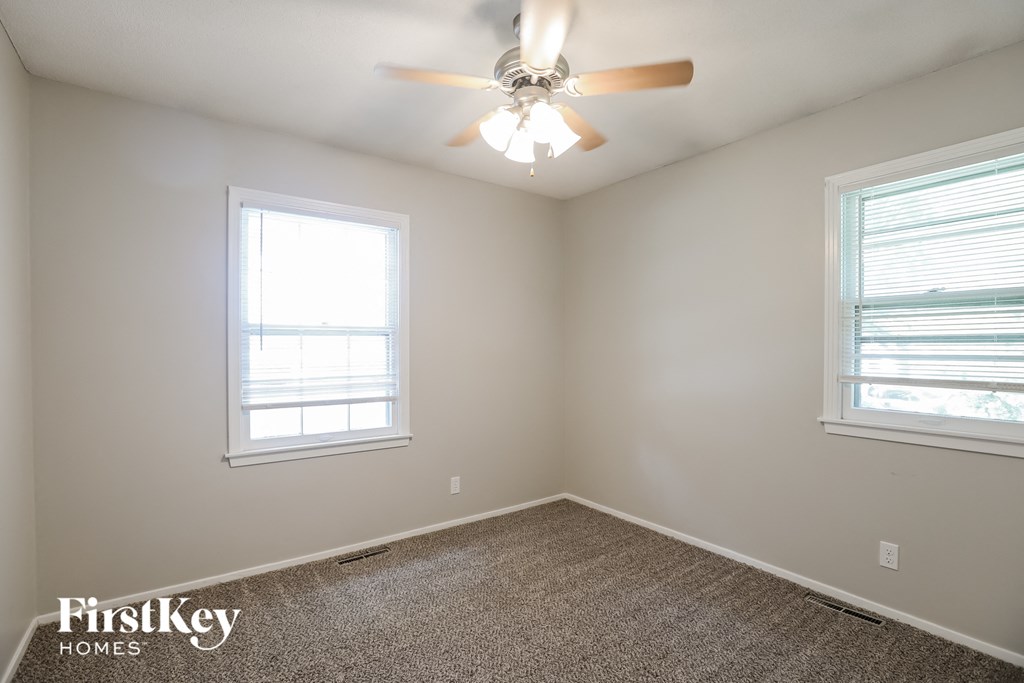 A room with a ceiling fan and two windows.