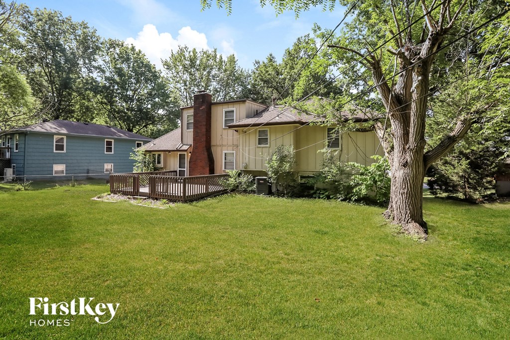 A tree stands in a grassy yard in front of two houses.