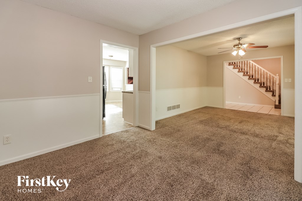 a carpeted living room with a staircase and a ceiling fan