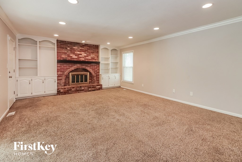 a carpeted living room with a brick fireplace and white shelves
