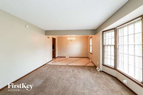 A spacious room with a carpeted floor and a window with blinds.