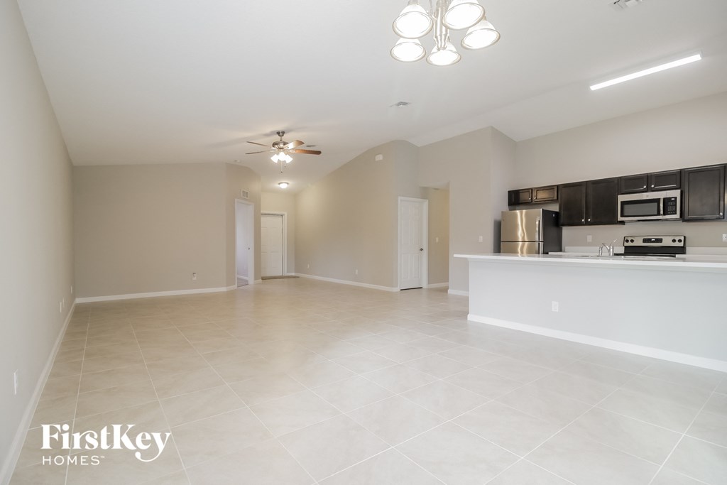an empty living room with a kitchen and a ceiling fan