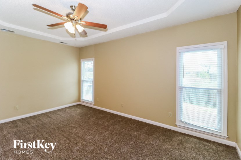 an empty living room with a ceiling fan and two windows