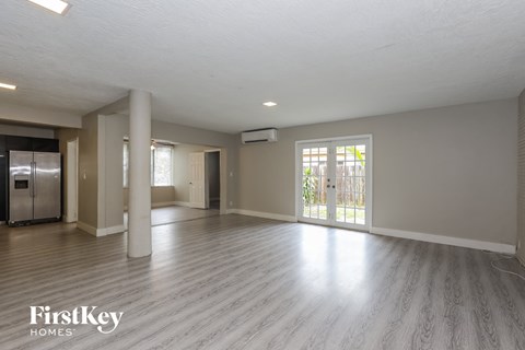 A spacious room with wooden flooring and a refrigerator in the corner.