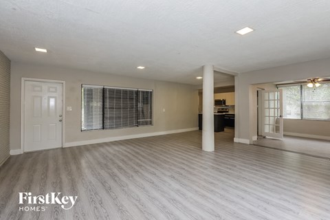 A spacious room with light grey flooring and white walls, with a door on the left and a window with blinds on the right.