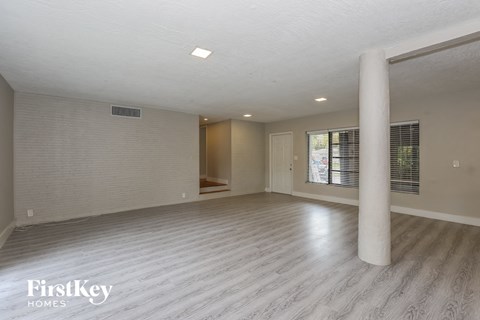 A spacious room with a light wooden floor and a large window with blinds.