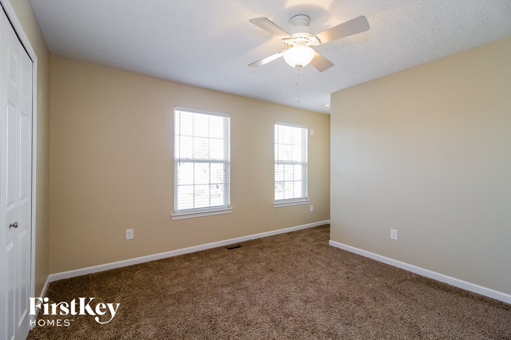 a carpeted living room with a ceiling fan and two windows