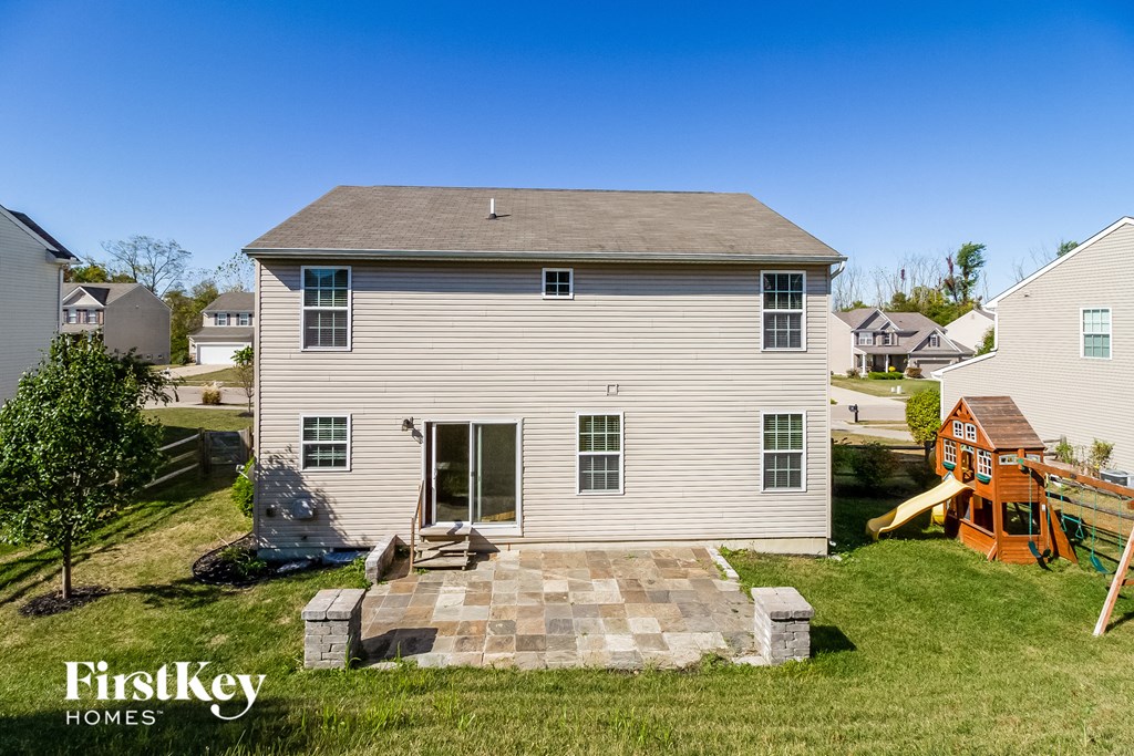 a backyard with a white house with a stone patio and a playground