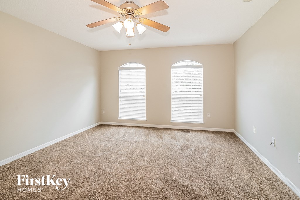 an empty living room with a ceiling fan and two windows