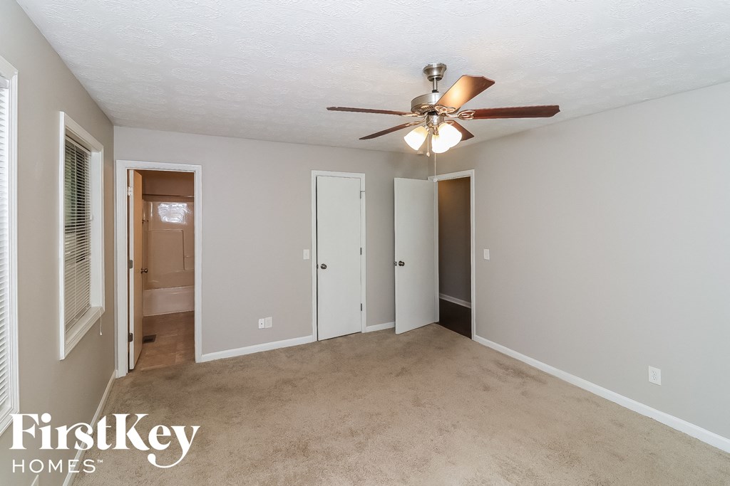 an empty living room with a ceiling fan and a door to a bathroom