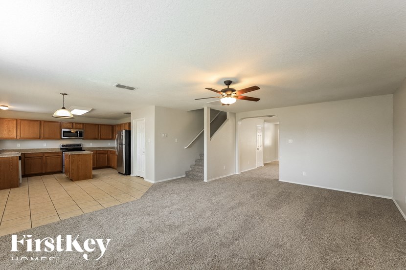 an empty living room with a ceiling fan and a kitchen
