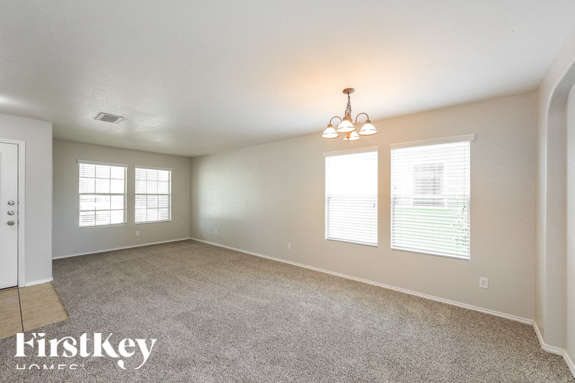 the living room of an empty house with carpet and a chandelier