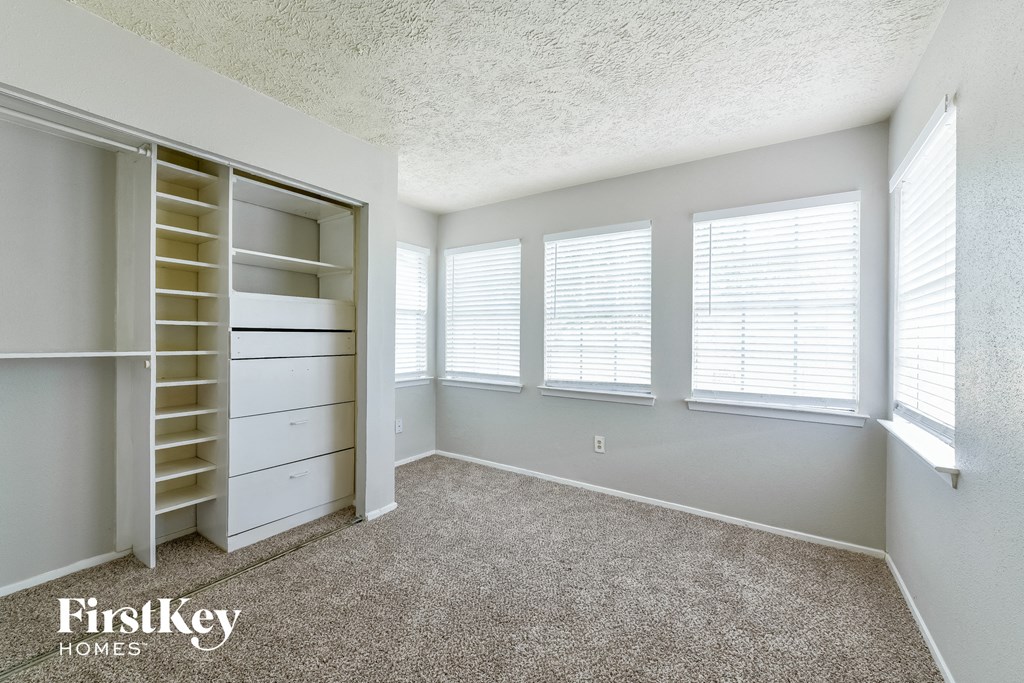 a bedroom with a closet and three windows and a carpeted floor