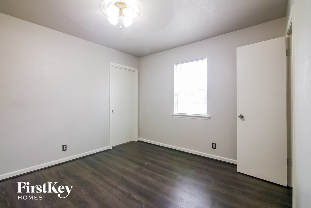 a bedroom with white walls and wood flooring and a window