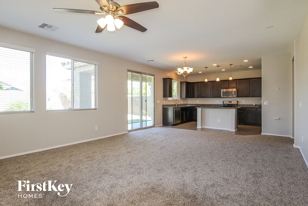 A spacious living room with a ceiling fan and a kitchen area in the background.
