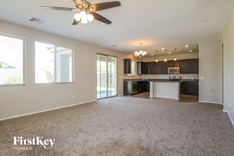 A spacious living room with a ceiling fan and a kitchen area in the background.