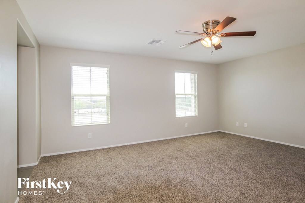 A spacious room with a ceiling fan and two windows.