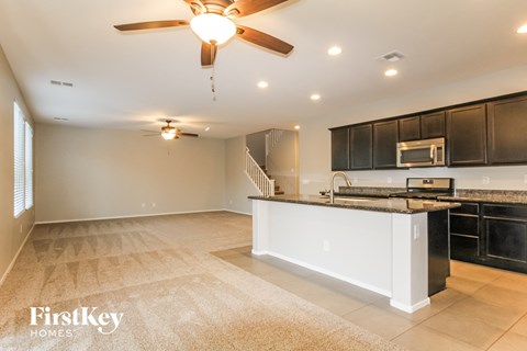 A spacious kitchen and living room with a ceiling fan and lighting fixtures.