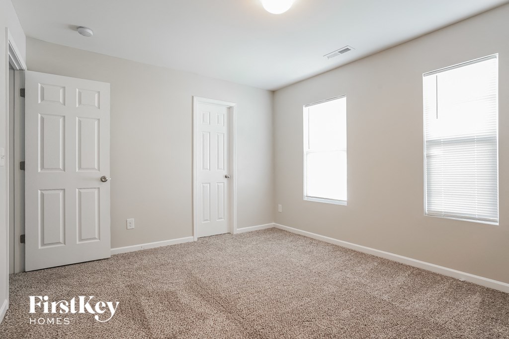a bedroom with a carpeted floor and two white doors and two windows