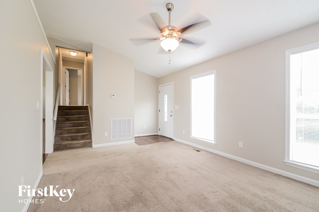 a spacious living room with carpet and a ceiling fan