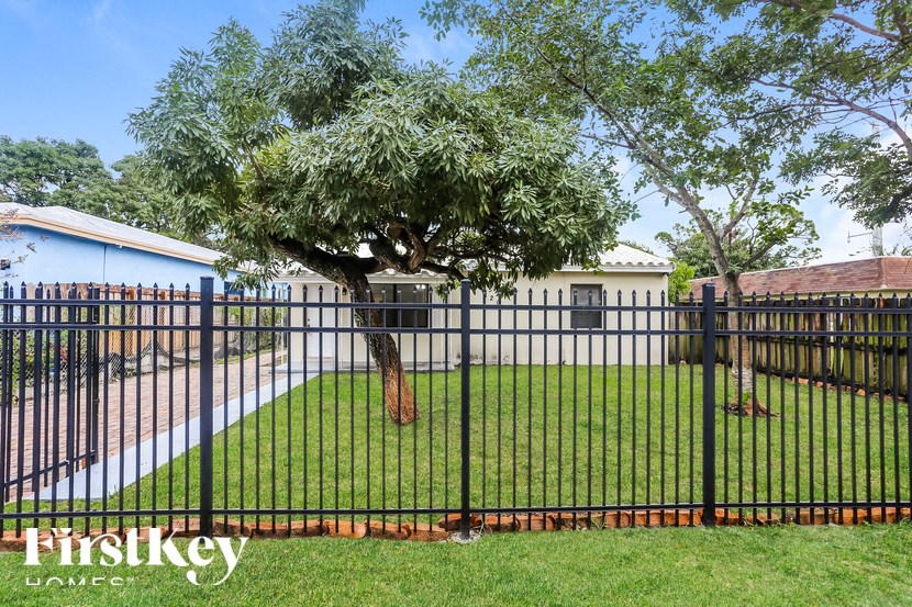 A black fence surrounds a green lawn with a tree in the middle.