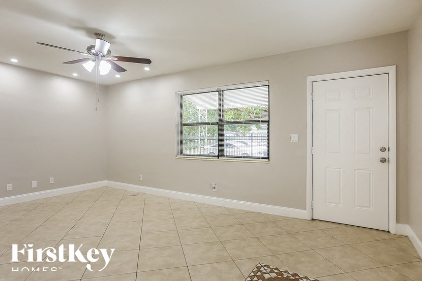 A room with a ceiling fan, a window with blinds, and a door.