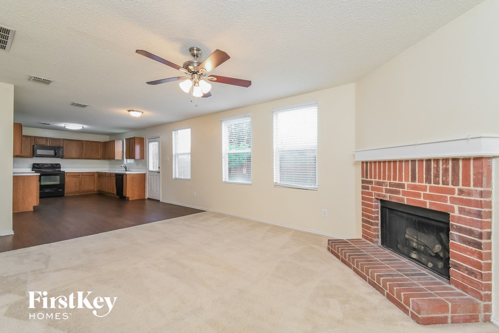 an empty living room with a brick fireplace and a ceiling fan