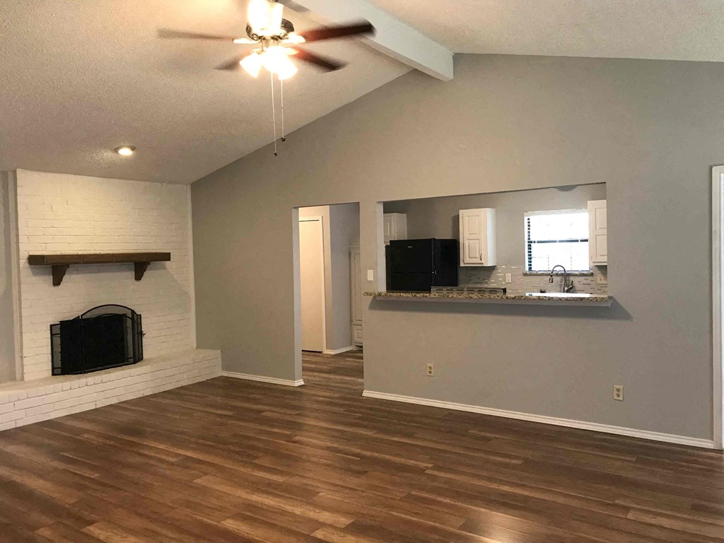 an empty living room with a fireplace and a kitchen
