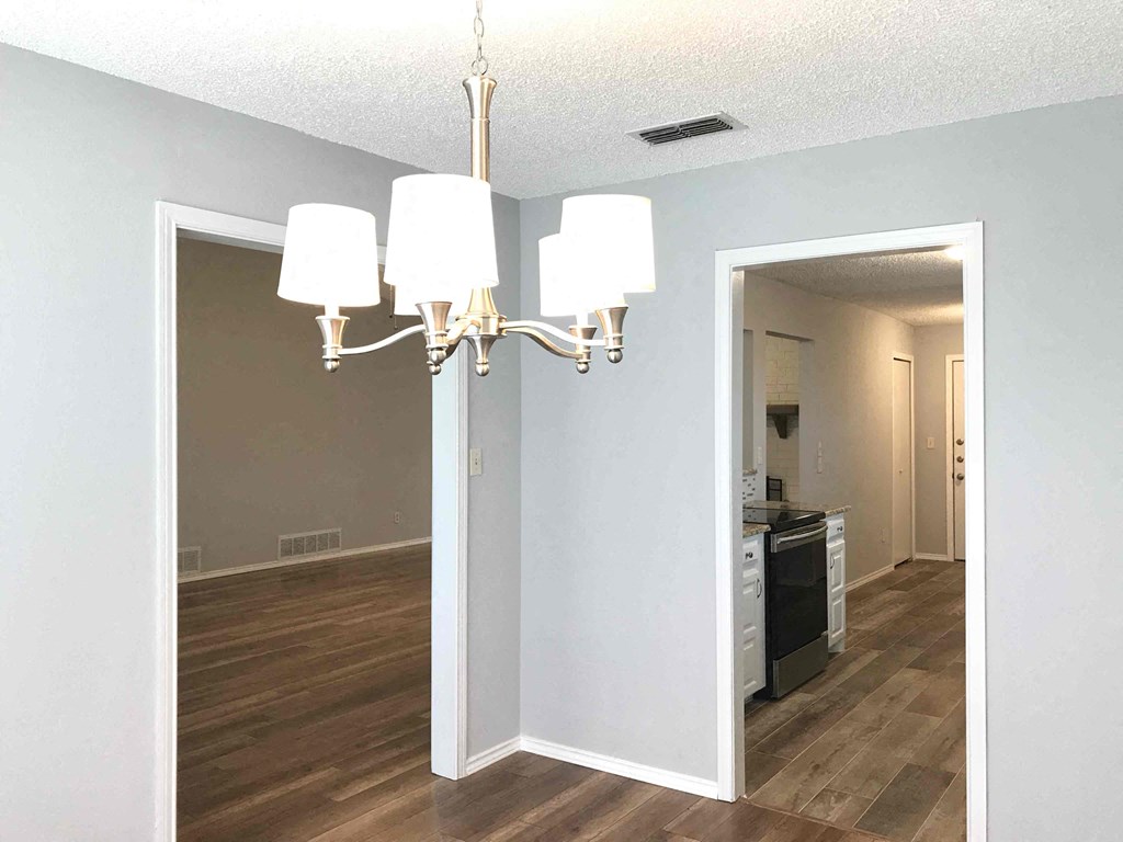 an empty living room with a chandelier and a kitchen