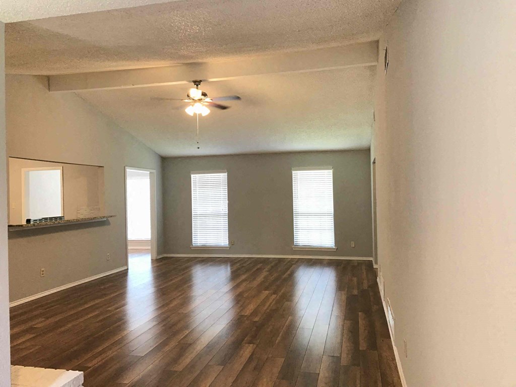 an empty living room with wood floors and a ceiling fan
