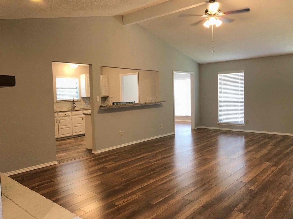 an empty living room with a kitchen and a ceiling fan